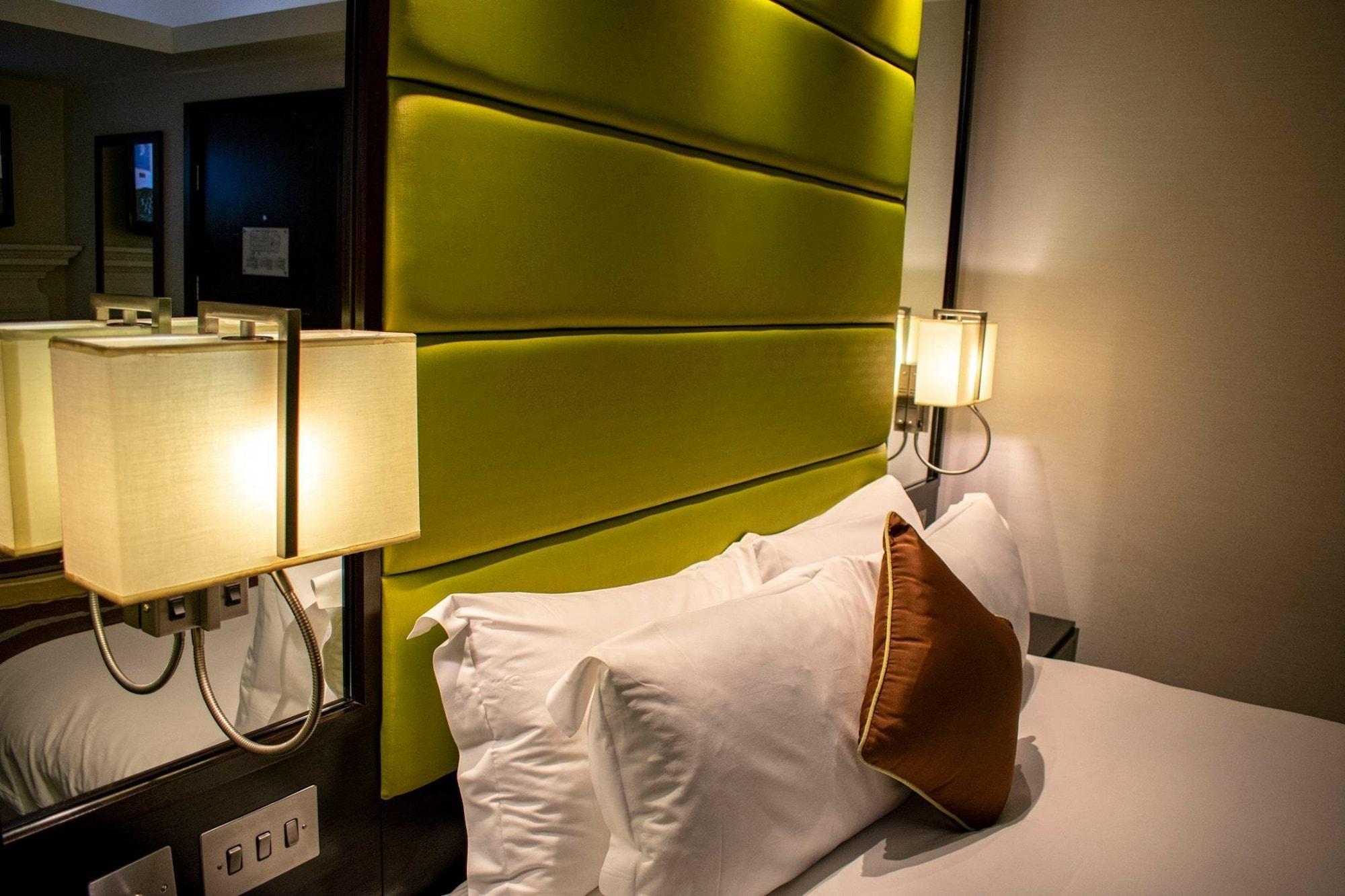 Hotel Montcalm Brewery Townhouse Londres Exterior foto The photo shows a modern hotel room with a stylish design. The focal point is a large bed with white pillows and a decorative brown pillow. The headboard is bright green and has a textured appearance. On either side of the bed, there are wall lamps t