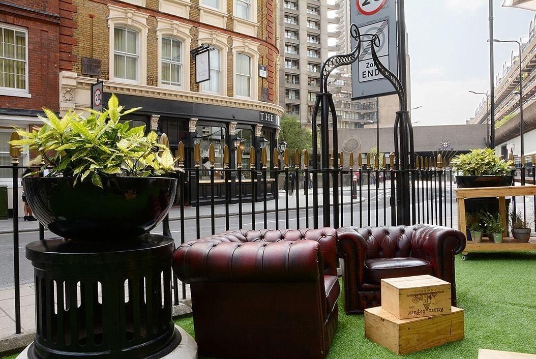 Hotel Montcalm Brewery Townhouse Londres Exterior foto The photo shows a street scene with a cozy outdoor seating area. There are two plush, dark leather couches arranged on green grass, creating a welcoming atmosphere. Surrounding the seating are large planters with vibrant plants. In the background, th