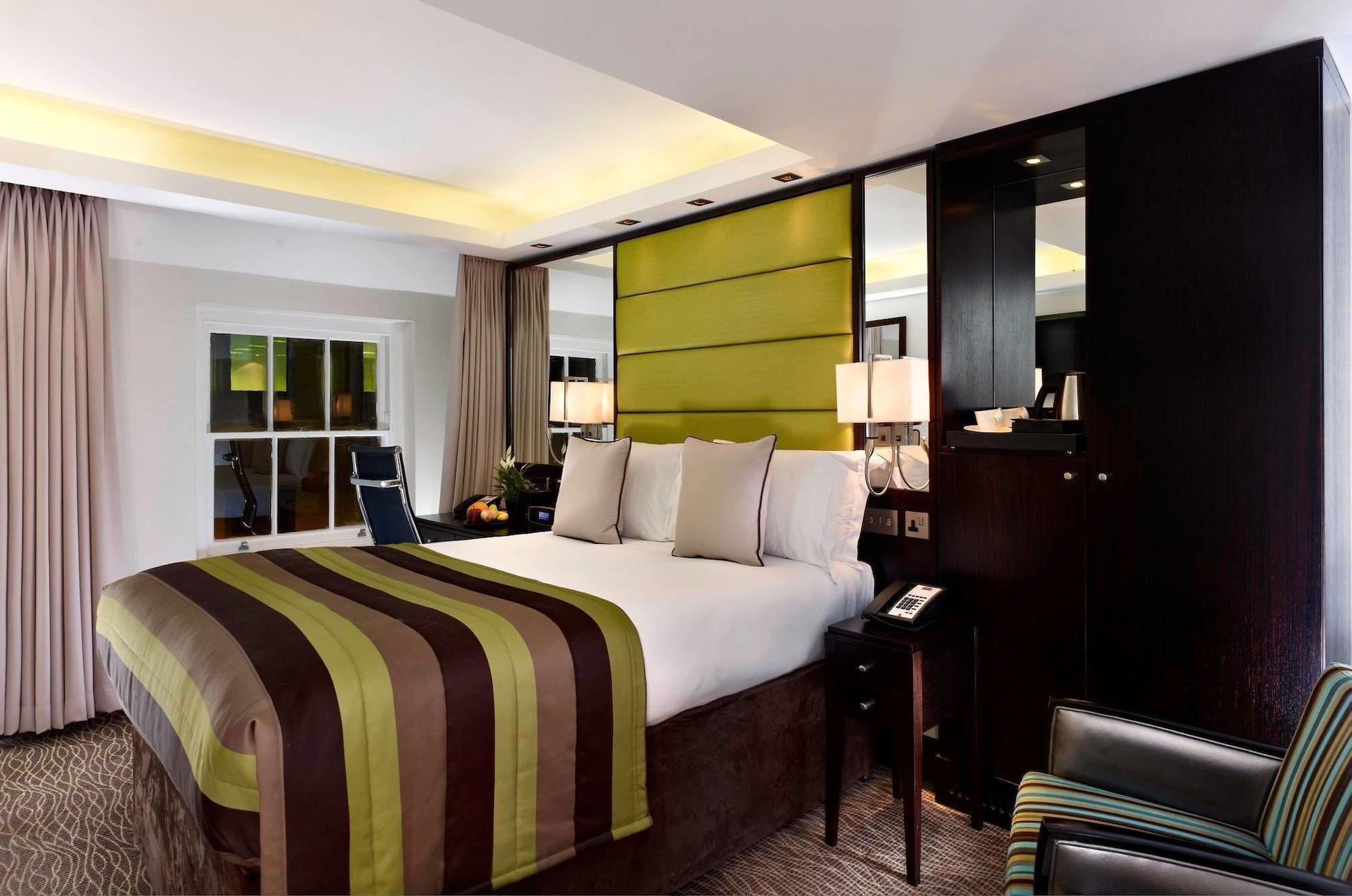 Hotel Montcalm Brewery Townhouse Londres Exterior foto The photo shows a modern hotel room featuring a large bed with a striped comforter in shades of green, brown, and cream. The bed is adorned with several decorative pillows. Behind the bed, there is a contemporary headboard with a green panel design. 