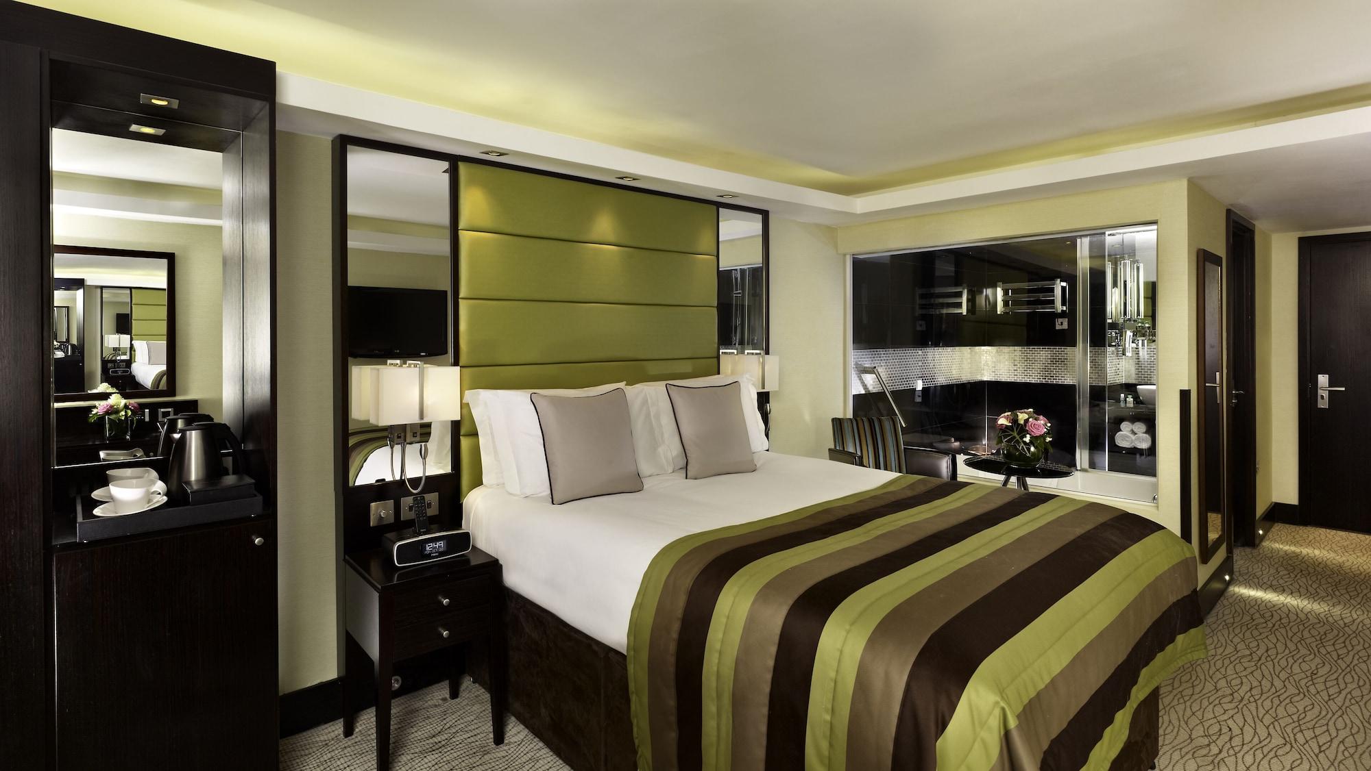 Hotel Montcalm Brewery Townhouse Londres Exterior foto The photo shows a modern hotel room designed with a sophisticated aesthetic. It features a comfortable double bed with a striped brown and green bedspread, complemented by two light gray decorative pillows. Behind the bed is an elegant headboard sect