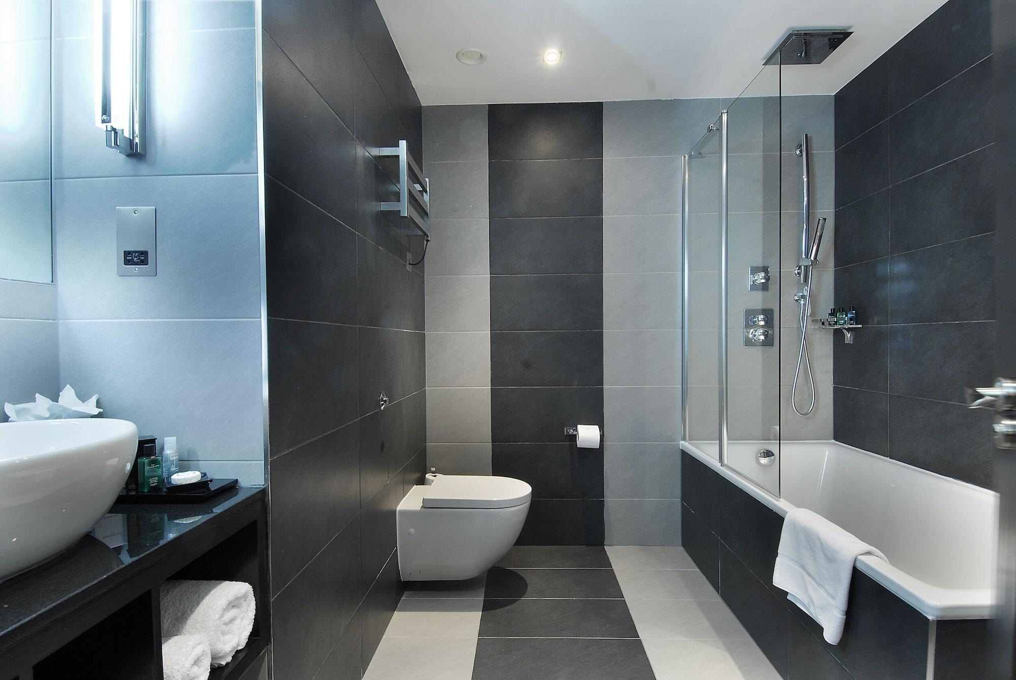Hotel Montcalm Brewery Townhouse Londres Exterior foto The photo shows a modern bathroom featuring a sleek design. The walls are tiled in a combination of dark gray and light gray, creating a contemporary look. On the left, there is a countertop with a basin and some toiletries placed on it. The middle s