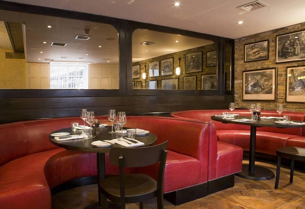 Hotel Montcalm Brewery Townhouse Londres Exterior foto The image shows the interior of a restaurant featuring a warm and inviting atmosphere. There are several round tables surrounded by black chairs, with red, upholstered booths lining the walls. The decor includes framed artwork hanging on the walls, a