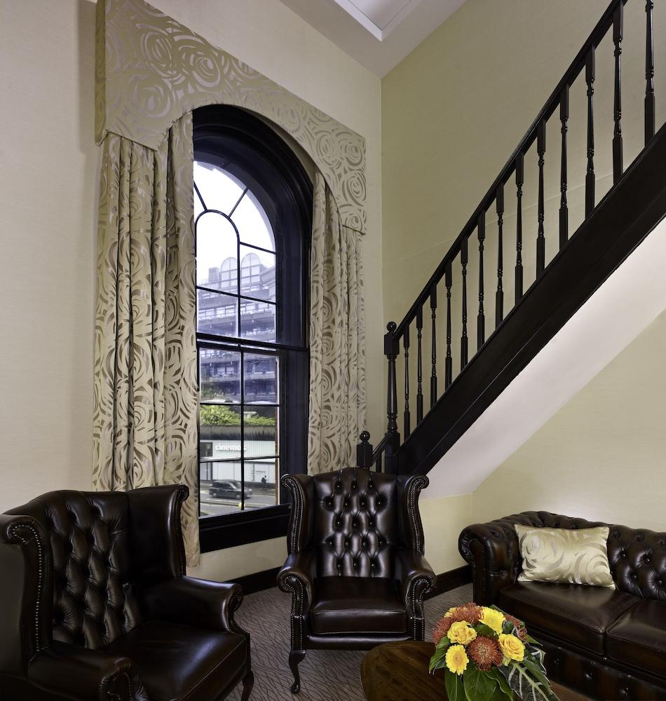 Hotel Montcalm Brewery Townhouse Londres Exterior foto The photo shows a cozy interior space featuring two elegant leather armchairs placed near a large, ornate window with arched top and decorative curtains. The wall is painted in a muted color, enhancing the warmth of the room. A staircase with black s