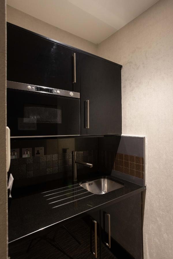 Hotel Montcalm Brewery Townhouse Londres Exterior foto The photo shows a modern kitchen setup with a dark color scheme. It features:

- A built-in microwave oven situated above a countertop.
- A sleek black cabinet beneath the microwave, which likely stores kitchen items.
- A stainless steel sink placed 