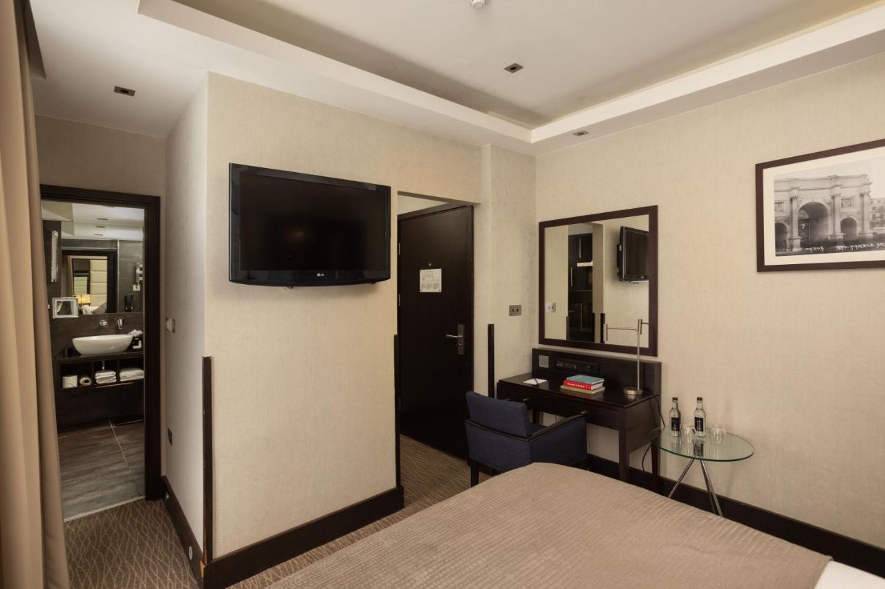 Hotel Montcalm Brewery Townhouse Londres Exterior foto The photo shows a hotel room featuring a double bed with a neutral-colored bedspread. On one wall, there is a flat-screen TV mounted. Adjacent to the bed, there is a stylish desk with a chair and a small glass table. A mirror is positioned above the 