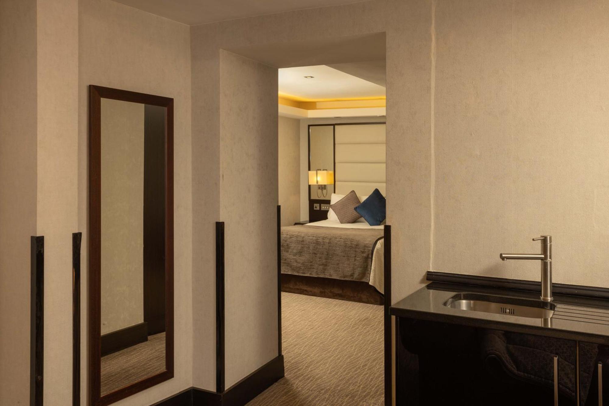 Hotel Montcalm Brewery Townhouse Londres Exterior foto The photo shows an interior space that appears to be part of a hotel room or suite. There is a doorway leading into a bedroom area, where a bed with decorative pillows is visible. In the foreground, there's a tall mirror on the left side and a small 