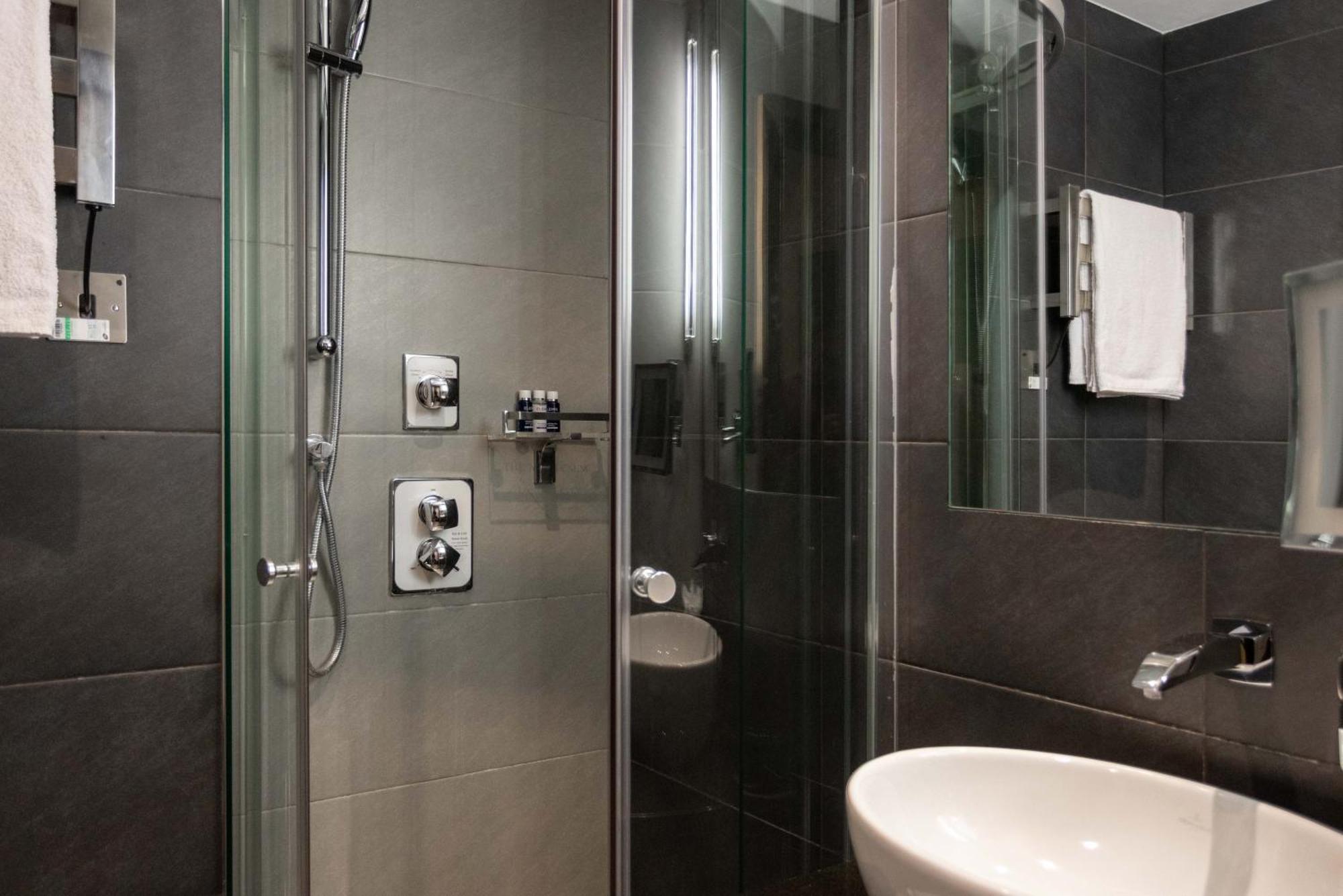 Hotel Montcalm Brewery Townhouse Londres Exterior foto The photo shows a modern bathroom with a glass shower enclosure. The shower features a handheld showerhead and various controls mounted on the wall. The walls are tiled in dark, sleek tones, contributing to a contemporary aesthetic. There is a round 