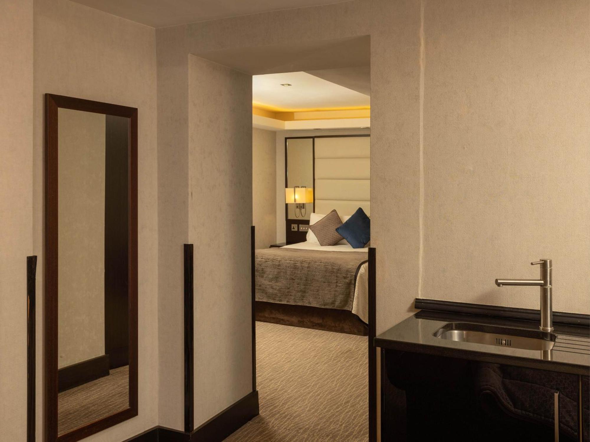 Hotel Montcalm Brewery Townhouse Londres Exterior foto The photo shows an interior space that appears to be a hotel room or a suite. There is a doorway leading to a bedroom visible in the background, where a bed with decorative pillows can be seen. To the side, there is a small wet bar or kitchenette are