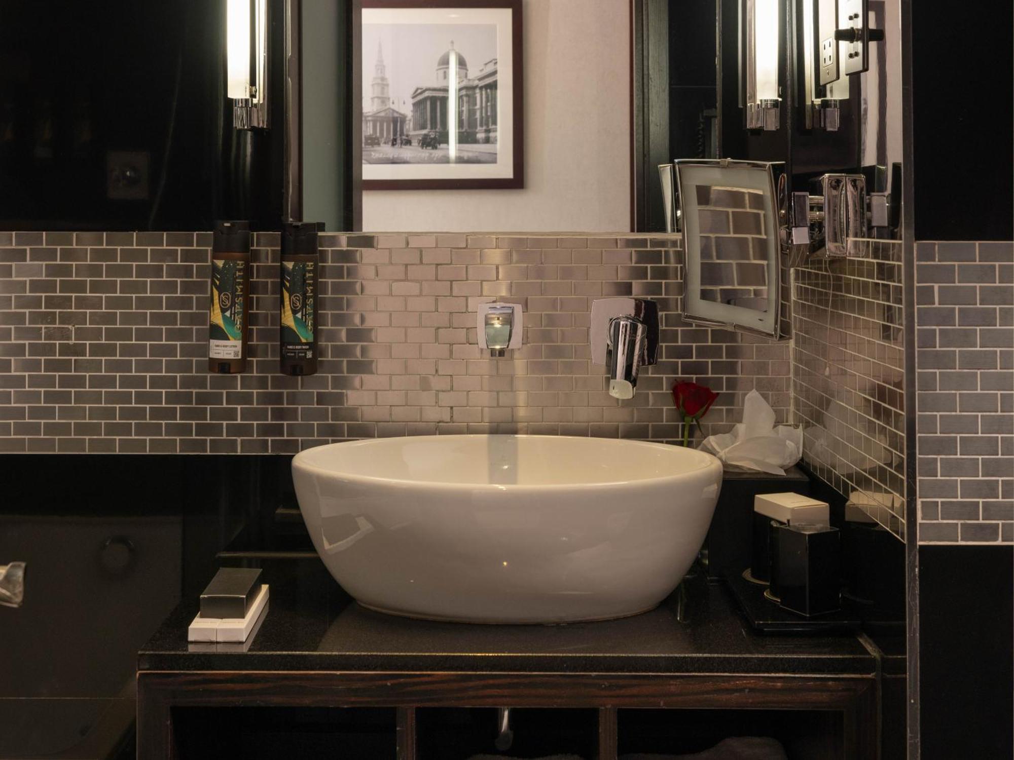 Hotel Montcalm Brewery Townhouse Londres Exterior foto The photo shows a modern bathroom with a stylish design. It features a large, round white sink placed on a dark wooden vanity. The walls are adorned with a mix of gray and silver tile, creating a sleek and contemporary look. Above the sink, there is 