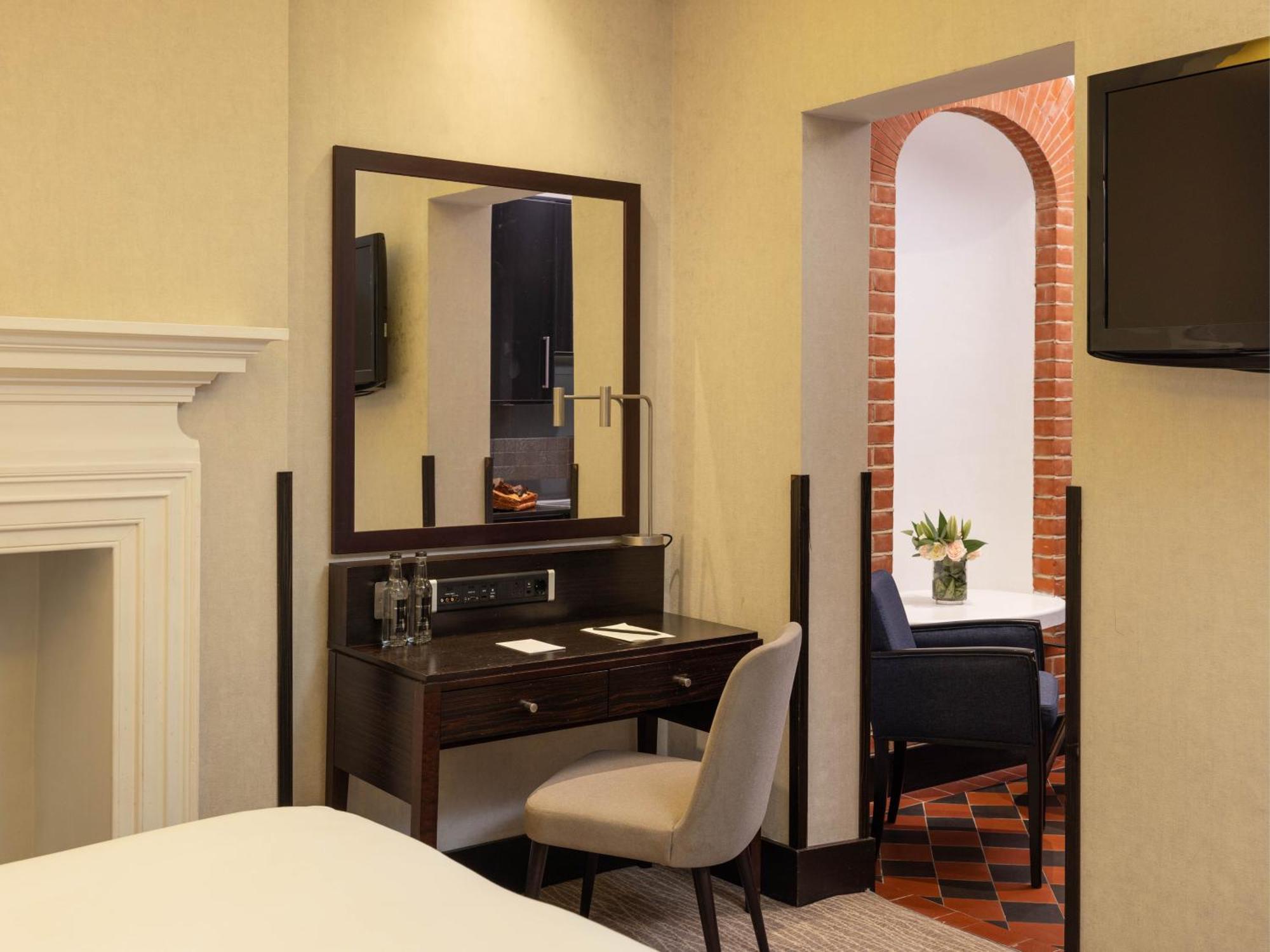 Hotel Montcalm Brewery Townhouse Londres Exterior foto The photo displays a hotel room setup. On the left side, there's a bed with a simple white bedding arrangement. Adjacent to the bed, there's a wooden desk with a chair, along with a mirror above the desk. The desk area is equipped with some glassware