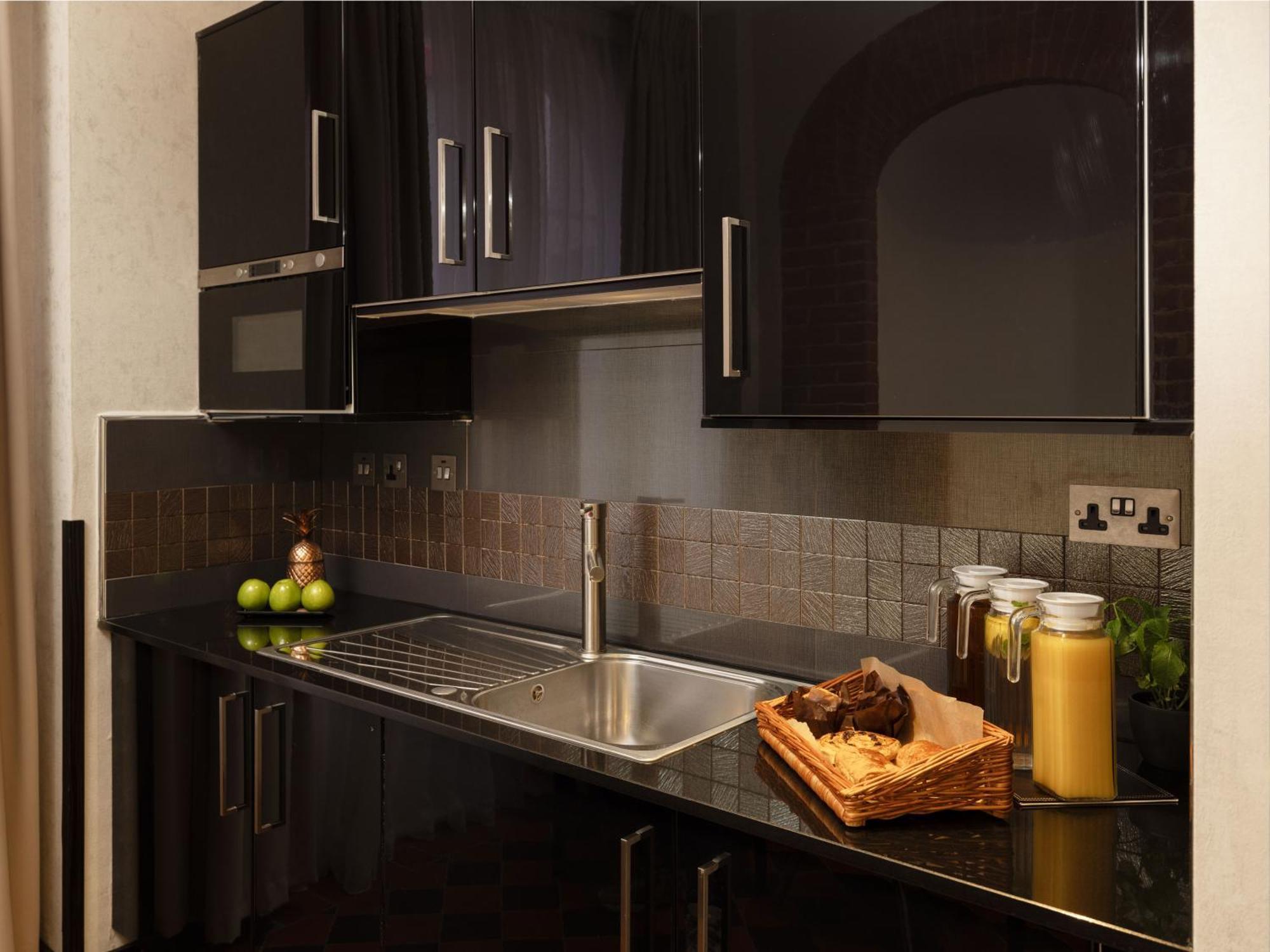Hotel Montcalm Brewery Townhouse Londres Exterior foto The photo shows a modern kitchen with sleek black cabinetry and a glossy finish. The kitchen features a stainless steel sink with a contemporary faucet, set against a dark, textured countertop. Above the counter, there are cabinets that match the cou