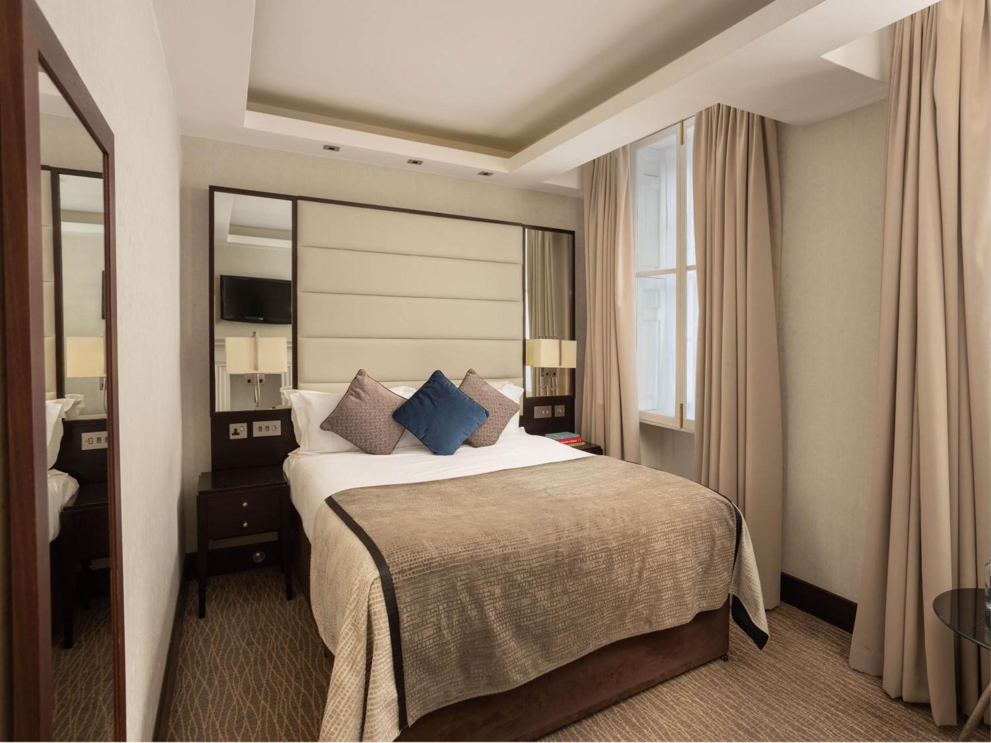 Hotel Montcalm Brewery Townhouse Londres Exterior foto The photo shows a cozy hotel room with a bed as the focal point. The bed is made with neutral-colored linens and has several pillows, including a decorative blue one. There are bedside tables on either side of the bed, each with a lamp. A large mirro