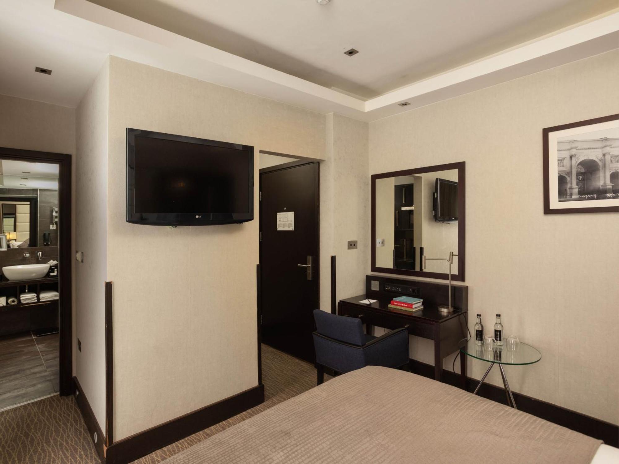 Hotel Montcalm Brewery Townhouse Londres Exterior foto The photo shows a hotel room with a modern and minimalist design. On the left, there's a wall-mounted flat-screen TV. In the center, there's a bed with a neutral-colored bedspread. To the right of the bed, there is a small desk with a mirror above it