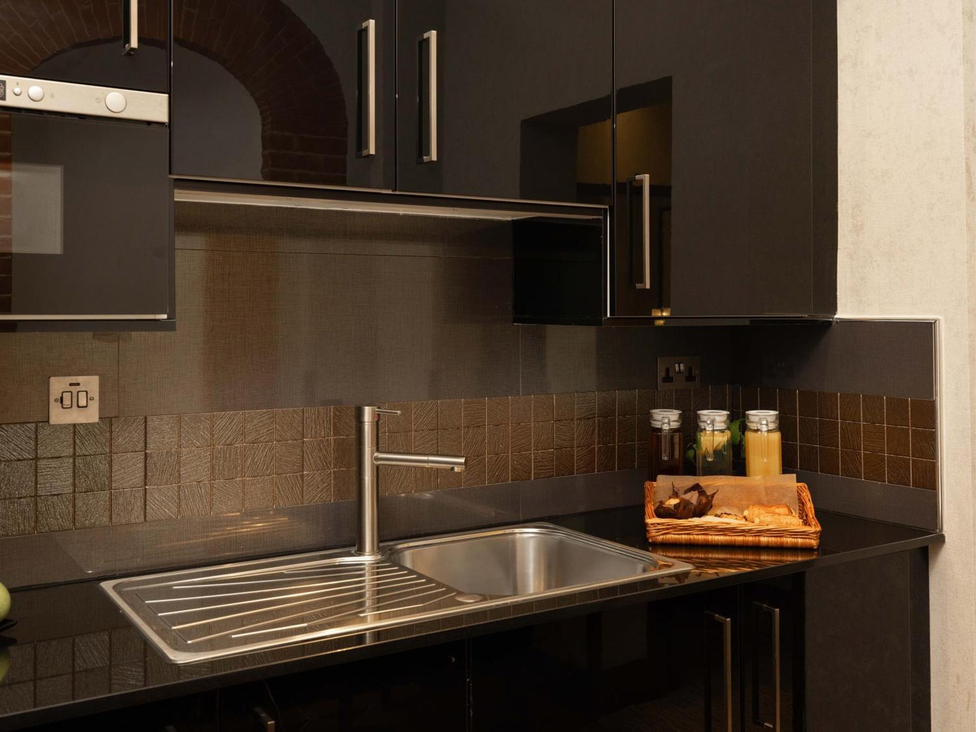 Hotel Montcalm Brewery Townhouse Londres Exterior foto The photo shows a modern kitchen with a sleek design. It features dark cabinetry with a glossy finish and stainless steel handles. There is a stainless steel sink with a simple faucet, and a countertop made of black material. Above the sink, there ar