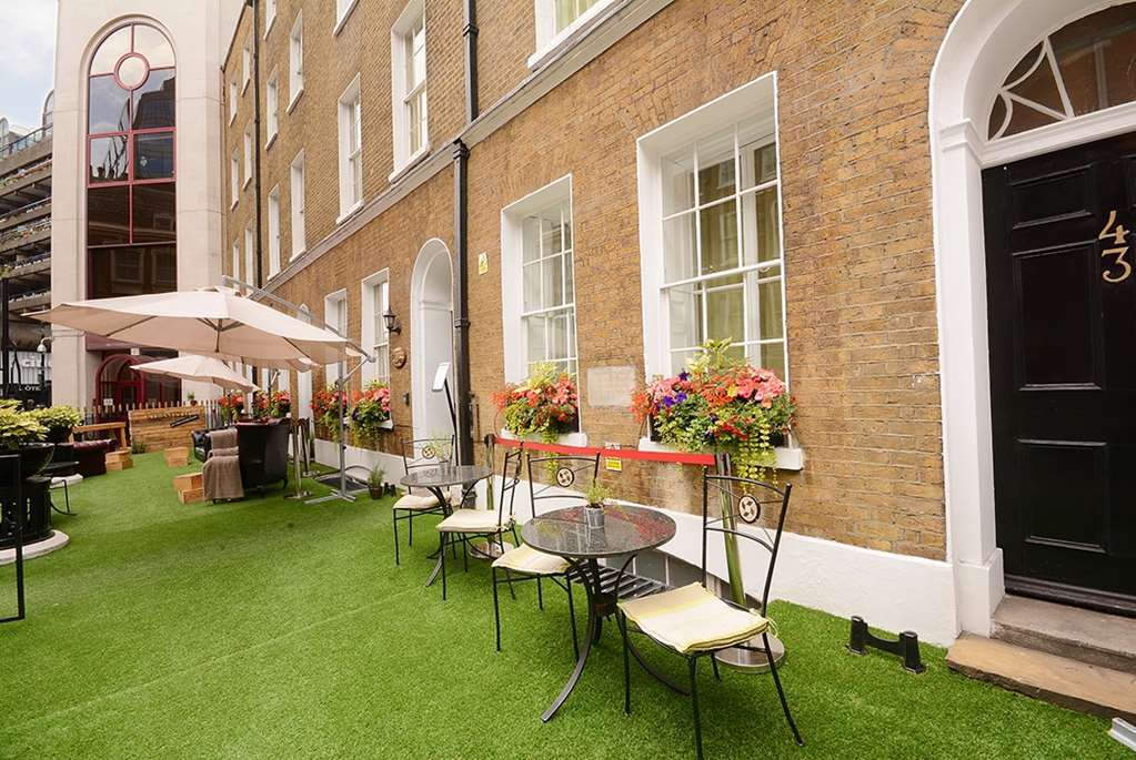 Hotel Montcalm Brewery Townhouse Londres Exterior foto The photo depicts a charming outdoor area in front of a building with a warm, textured brick facade. There is a neatly maintained lawn, likely made of artificial grass, and several small round tables with chairs are arranged outside. Flower pots with