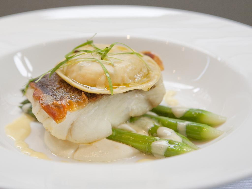 Hotel Montcalm Brewery Townhouse Londres Exterior foto The image shows a beautifully presented dish featuring a piece of fish, likely a white fish, topped with a clam. It is served on a bed of green asparagus spears. The dish is garnished with thinly sliced herbs or greens, adding a touch of color. The s