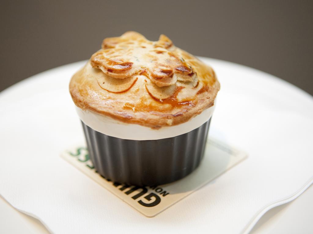 Hotel Montcalm Brewery Townhouse Londres Exterior foto The photo shows a small, individual serving of a pie, likely a savory dish. It has a golden-brown crust with decorative elements on top, resembling leaves or floral patterns. The pie is served in a black dish and placed on a white plate. The overall 