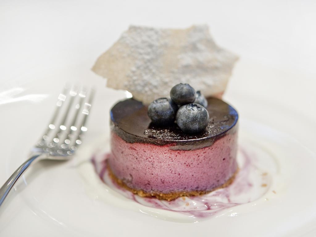Hotel Montcalm Brewery Townhouse Londres Exterior foto The photo shows a beautifully plated dessert, which appears to be a round cheesecake or mousse. It has a pinkish-purple filling, topped with a glossy dark chocolate layer. Three fresh blueberries sit on top, adding a pop of color. The dessert is acco