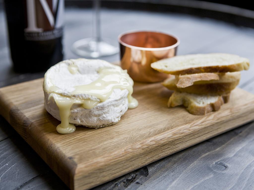 Hotel Montcalm Brewery Townhouse Londres Exterior foto The photo features a wooden serving board with several items. There is a round cheese, likely Brie or a similar soft cheese, that appears to be melting and dripping slightly. Next to the cheese, there is a small copper cup that might contain a sauce 