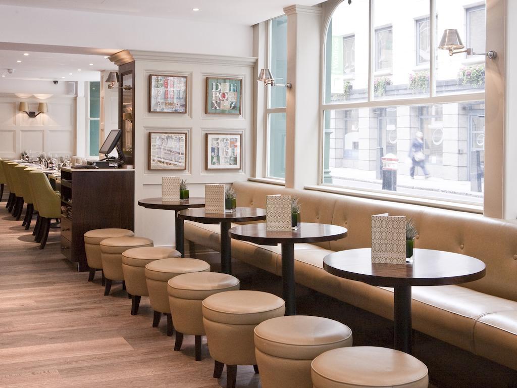 Hotel Montcalm Brewery Townhouse Londres Exterior foto The photo displays a modern café or restaurant interior. There is a cozy seating area featuring light-colored, upholstered benches along the wall, accompanied by small round tables. The tables are paired with circular stools. The decor includes frame