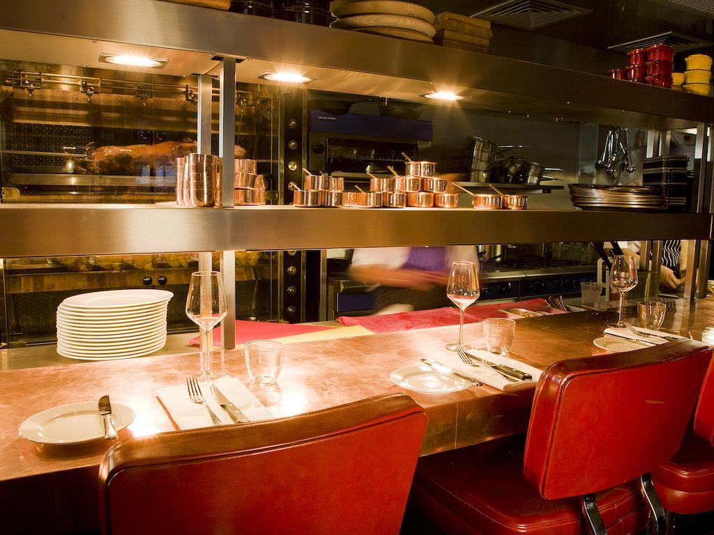 Hotel Montcalm Brewery Townhouse Londres Exterior foto The photo shows a restaurant interior featuring a bar or counter area. There are red chairs arranged around a copper-topped table where dining utensils and plates are set. Above the counter, there are shelves displaying various cooking pots and kitch