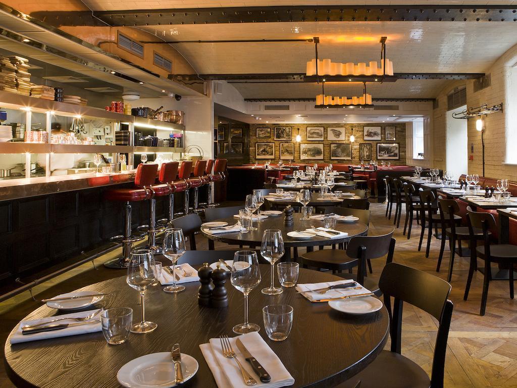 Hotel Montcalm Brewery Townhouse Londres Exterior foto The photo shows the interior of a stylish restaurant. It features several round tables set with white plates, glasses, and silverware, all neatly arranged for dining. The decor includes a modern design with wooden floors and a mix of lighting fixture