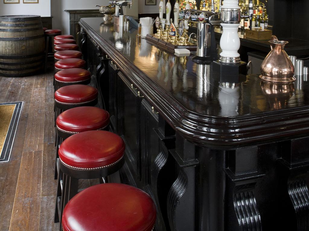Hotel Montcalm Brewery Townhouse Londres Exterior foto The photo shows a bar setting with a long, polished dark wooden bar counter. Attached to the counter are several bar stools with red leather seats. Behind the bar, there are various bottles, suggesting a well-stocked bar. The flooring appears to be w