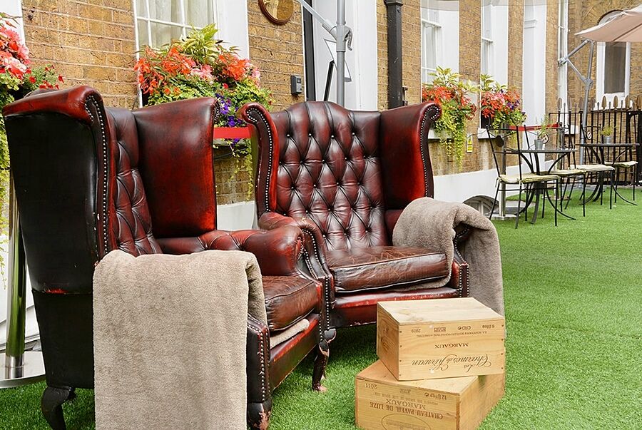 Hotel Montcalm Brewery Townhouse Londres Exterior foto The photo depicts two large, elegant armchairs with a classic design, featuring rich burgundy leather upholstery and button tufting. They are positioned in a cozy outdoor setting, with lush green artificial grass beneath them. Next to the chairs, the