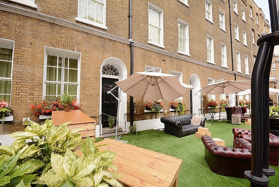 Hotel Montcalm Brewery Townhouse Londres Exterior foto The photo depicts an outdoor area of a building with a brick facade. There are several large windows visible, along with a wooden door. The setting features outdoor furniture, including couches in a dark leather finish and wooden tables. Large umbrel